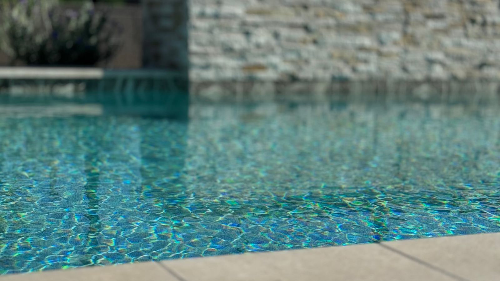 Sunlit, rippling pool water in front of a stacked-stone wall