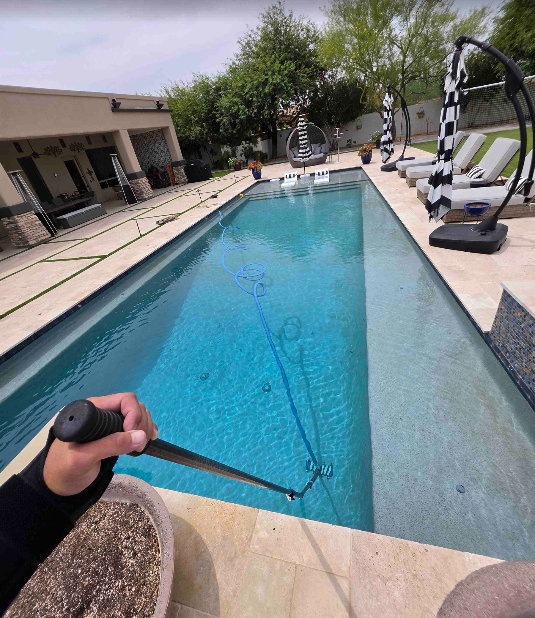 Vacuuming a long backyard pool with clear blue water