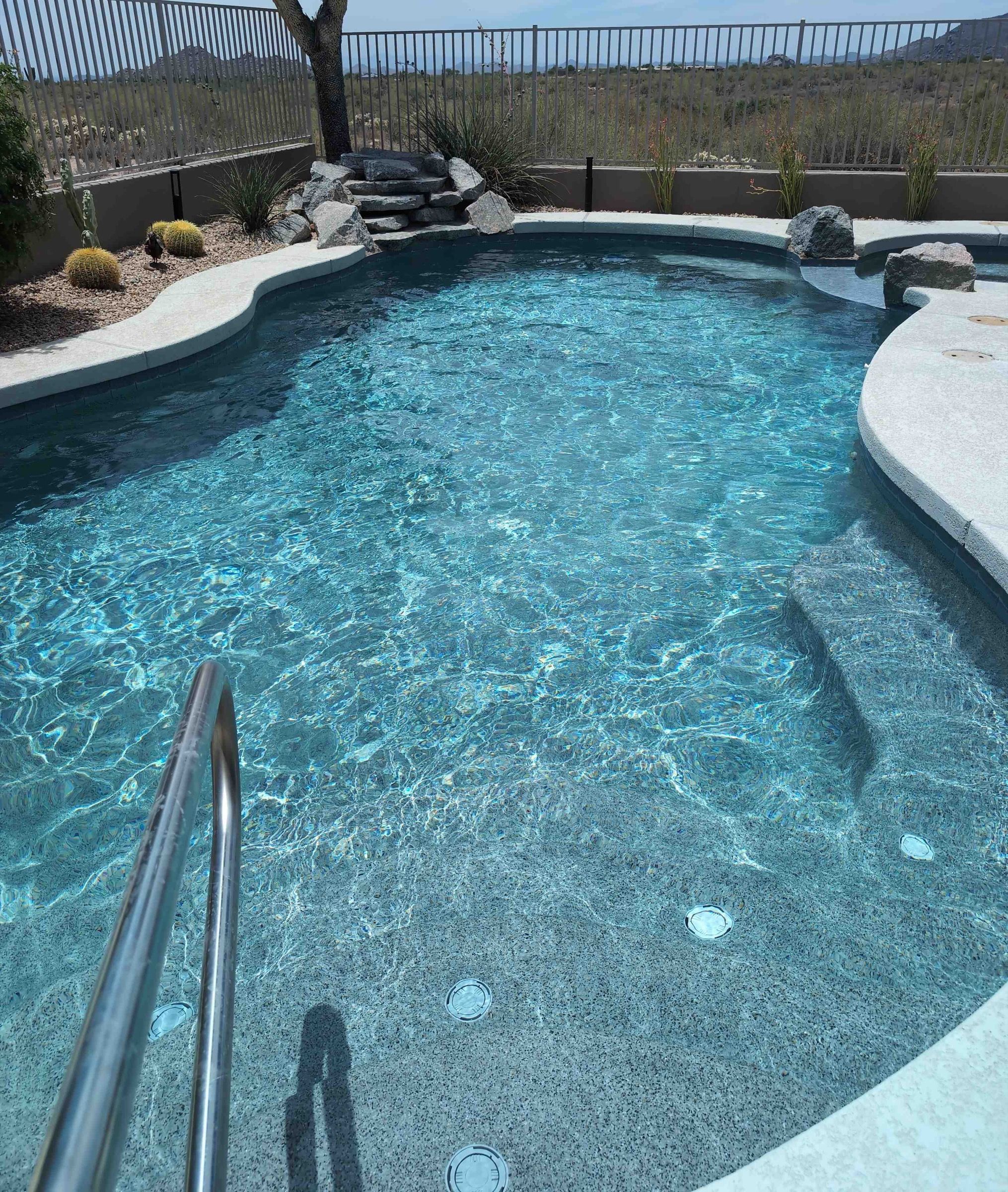 A clear, curving backyard pool with steps and a rock waterfall in the desert