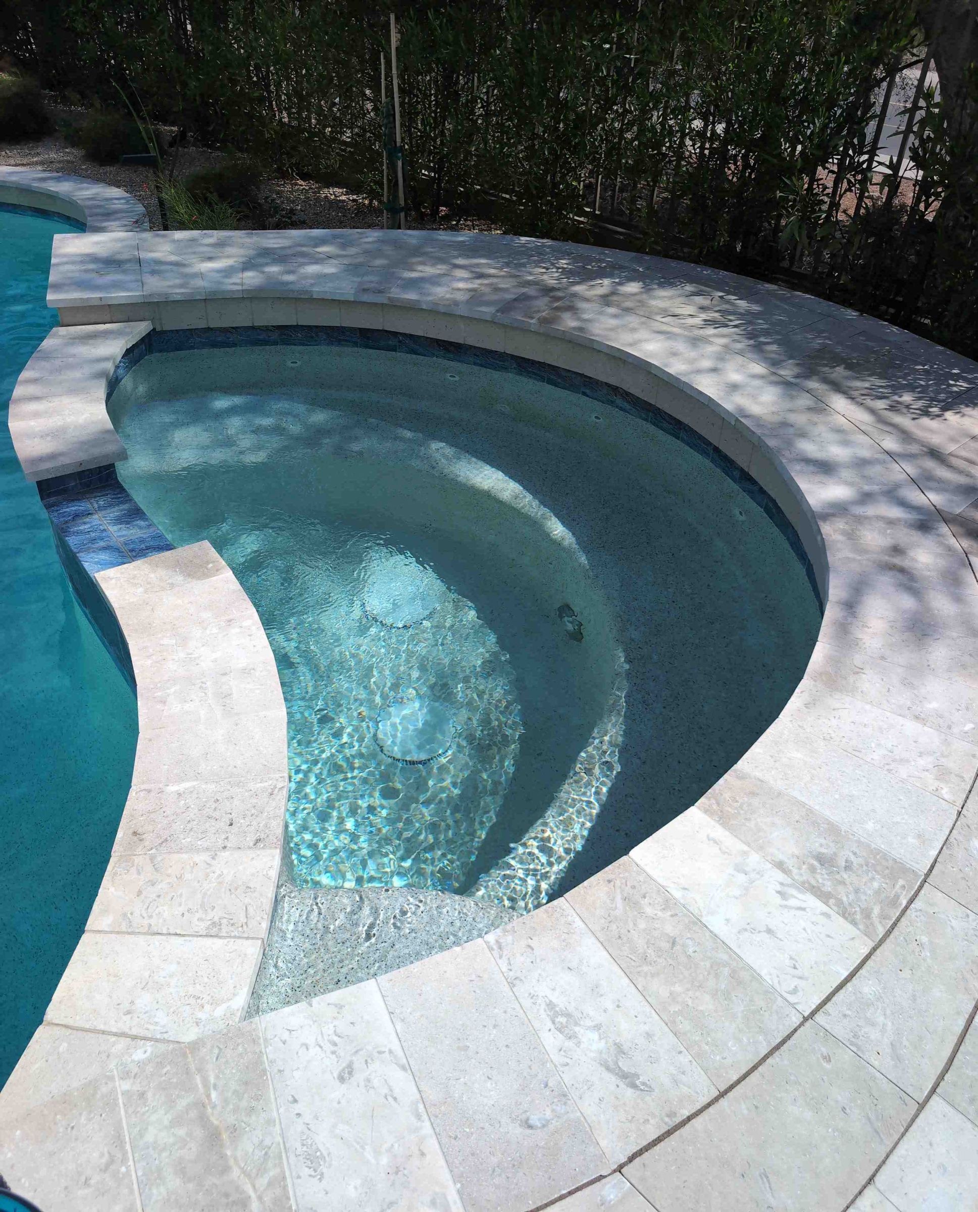 A round spa with travertine coping and clear blue water